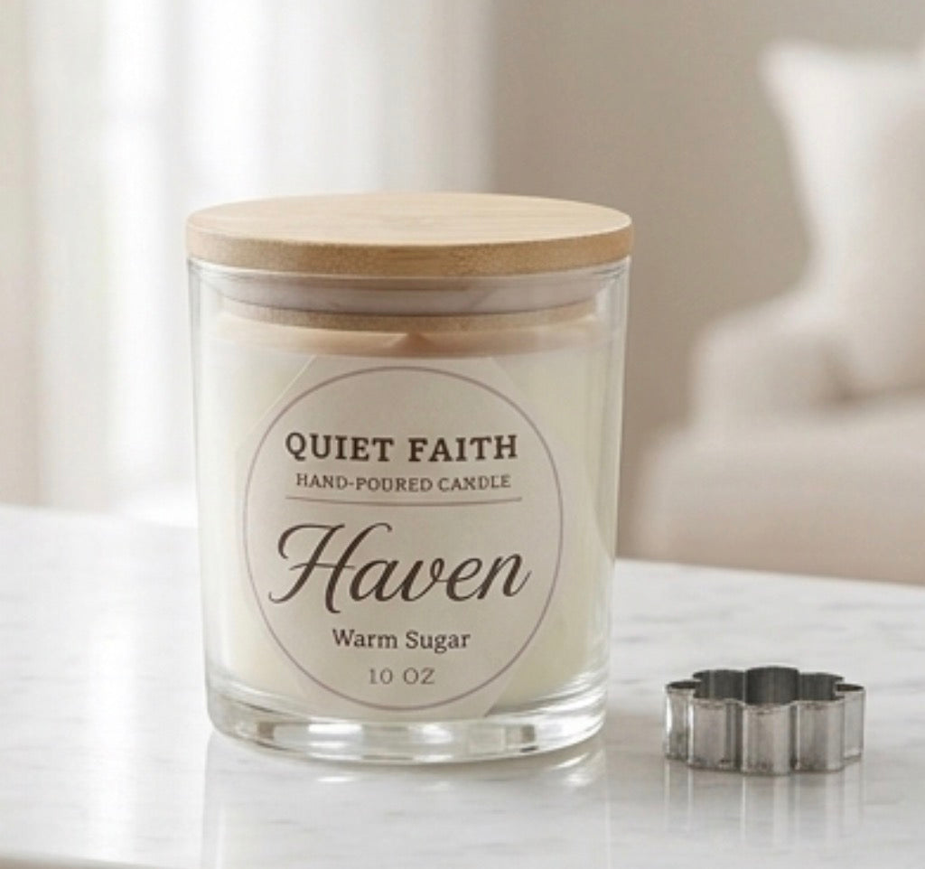 A 10 oz glass jar candle with a light wood lid and a white label reading 'QUIET FAITH HAND-POURED CANDLE Haven Warm Sugar 10 OZ'. A small silver flower-shaped metal tray sits beside it on a light marble surface, with a softly blurred indoor background.